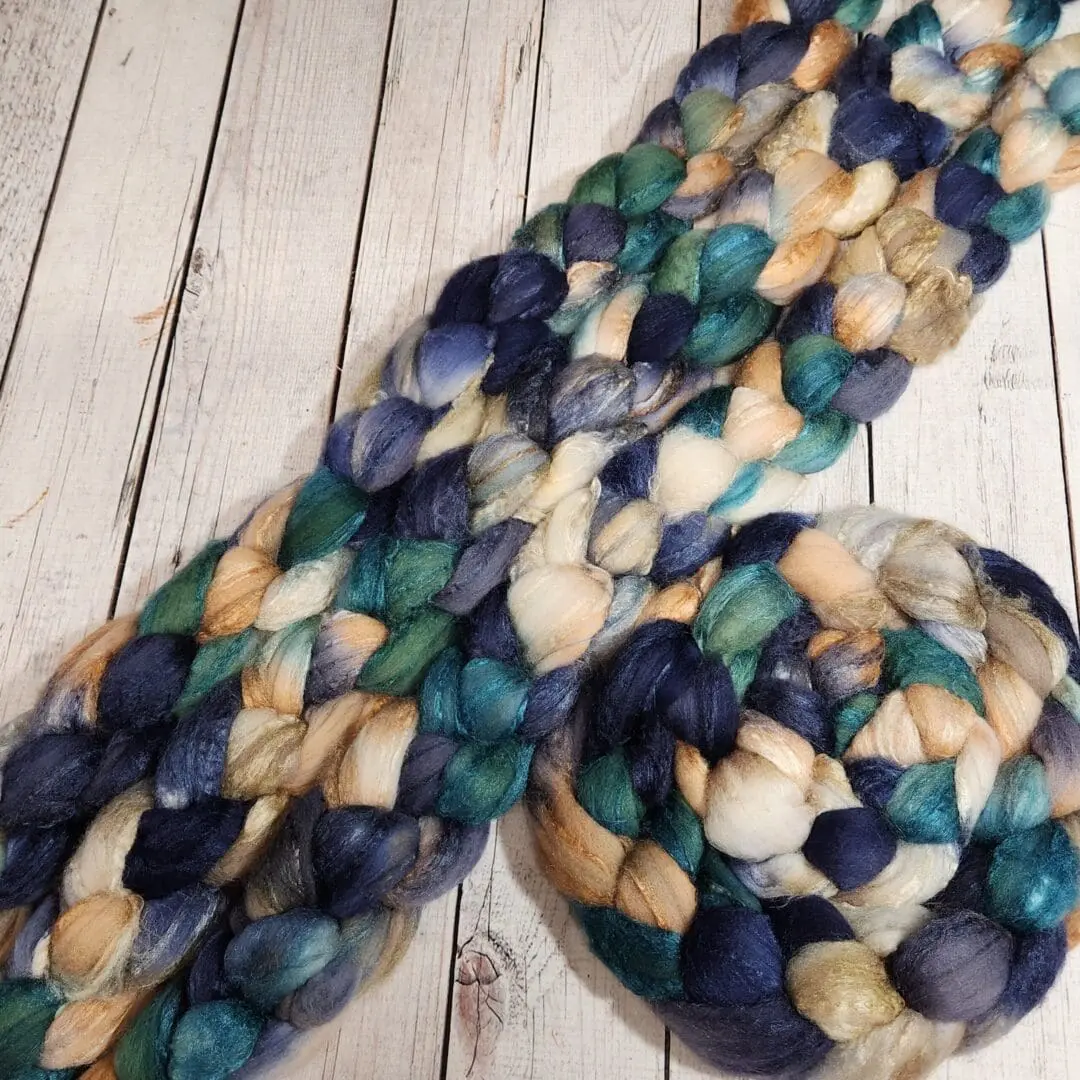 A skein of blue and green roving on a wooden table.
