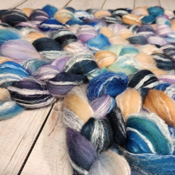 A skein of blue, purple, and yellow fibers on a wooden floor.