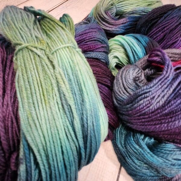 Skeins of purple, blue and green yarn on a wooden table.