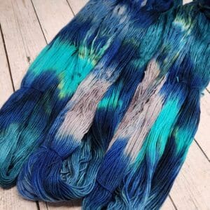 Skeins of blue and grey dyed yarn on a wooden floor.