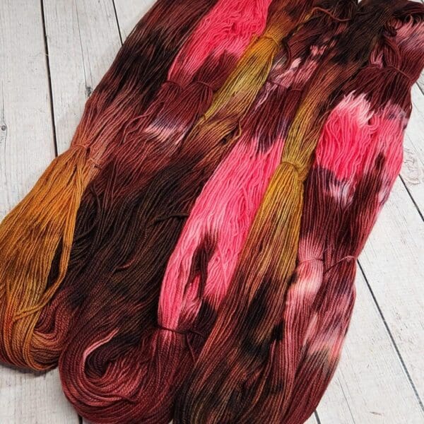 Four skeins of dyed yarn on a wooden floor.
