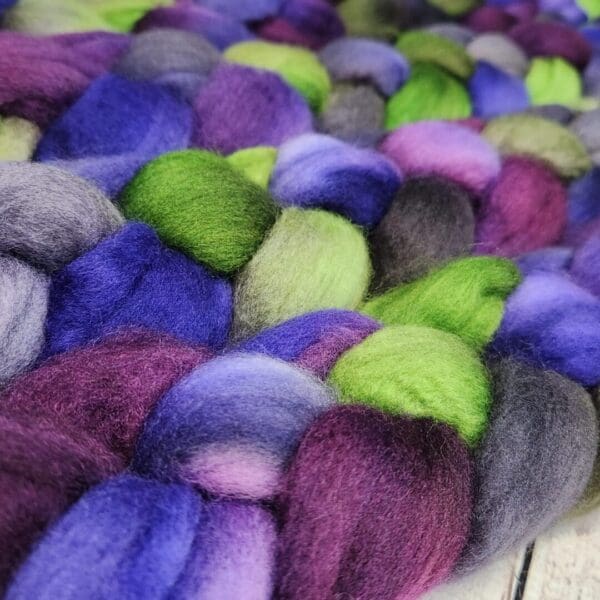 Purple and green wool roving on a wooden table.