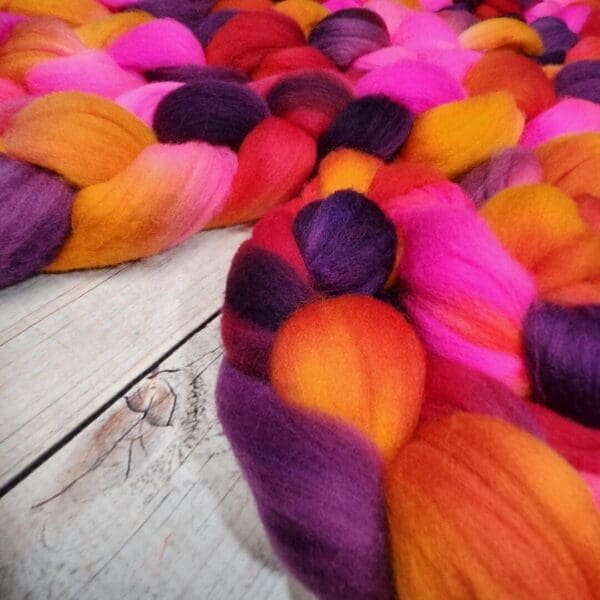 A bunch of colorful roving laying on a wooden floor.