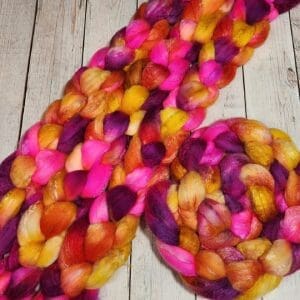 A skein of Rows of Tulips ~ 100g Hand-Dyed Luxury Combed Top Fiber on a wooden table.