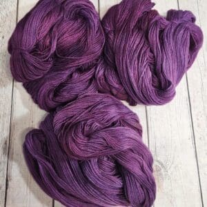 Three skeins of purple yarn on a wooden table.