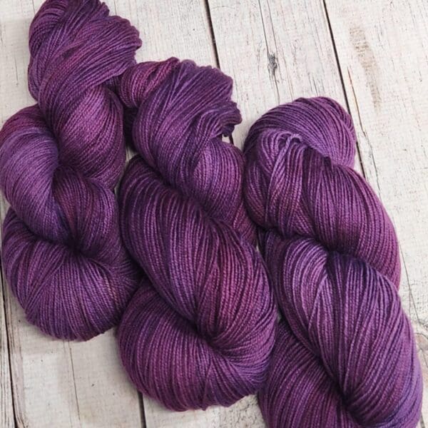 Three purple skeins on a wooden table.