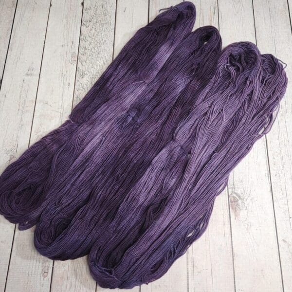 Three skeins of purple yarn on a wooden floor.