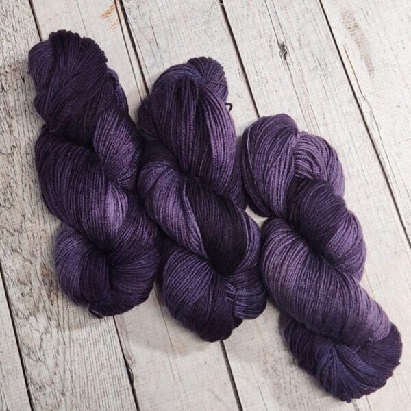 Three purple skeins on a wooden floor.