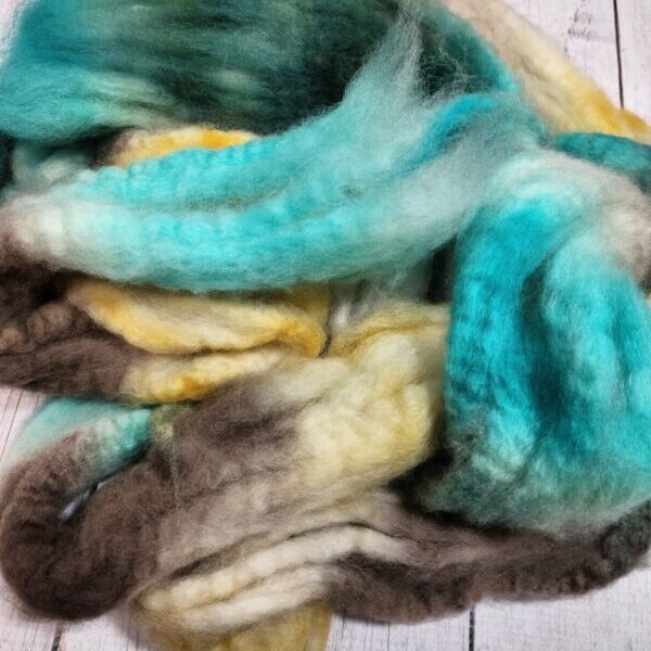 A pile of Disco Date ~ 100g Hand-Dyed Luxury Combed Top Fiber on a wooden floor.
