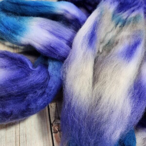 A bunch of Disco Date ~ 100g Hand-Dyed Luxury Combed Top Fiber on a wooden table.