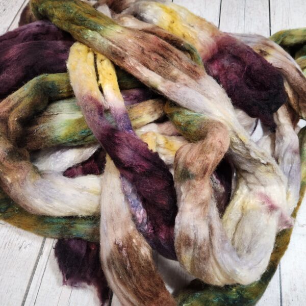 A bunch of Disco Date ~ 100g Hand-Dyed Luxury Combed Top Fiber on a wooden floor.